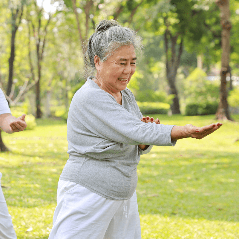 mujer de edad avanzada con pelo blanco ejecutando un ejercicio de chi kung en la naturaleza.